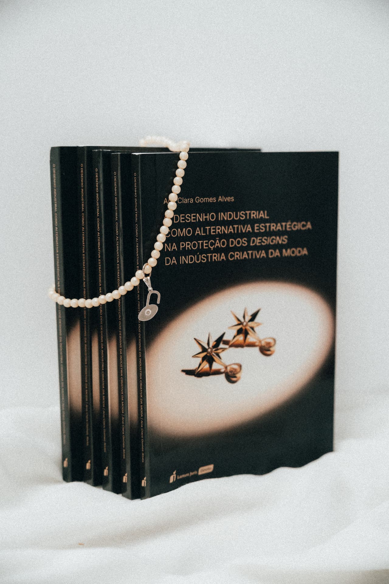 Exemplares do livro O Desenho Industrial na moda com colar de pérolas